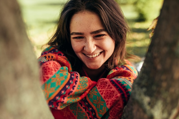 Porträt einer glücklichen brünetten jungen Frau mit Sommersprossen, die lächelt und das Wetter mit einem Pullover auf Naturhintergrund genießt Stilvolle weibliche lächelnde Pose im Park an einem sonnigen Tag