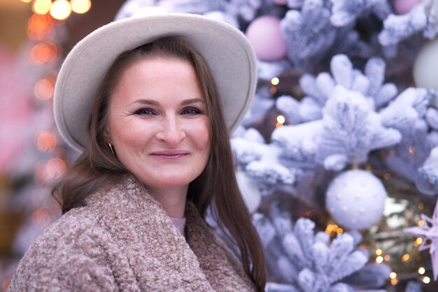 Porträt einer glücklichen erwachsenen Frau mittleren Alters in der Nähe des Weihnachtsbaums mit Geschenkbox