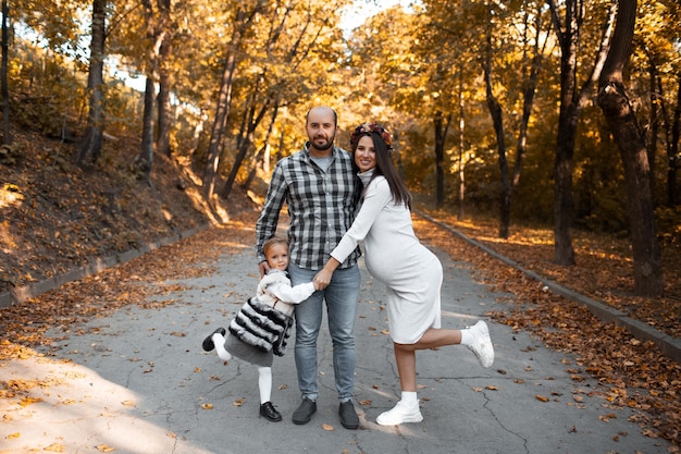 Porträt einer glücklichen Familie auf dem Hintergrund des goldenen Parks am Herbsttag Vater, Tochter und schwangere Mutter