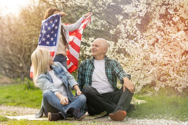 Porträt einer glücklichen Familie, die am 4. Juli den Unabhängigkeitstag feiert und die Silhouette der US-Nationalflagge gegen den Park hält