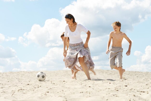 Porträt einer glücklichen Familie, die am Sommertag am Strand Fußball spielt