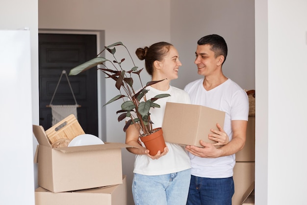 Porträt einer glücklichen Familie, die mit Kisten und Pflanzen im Blumentopf steht, sich sanft und liebevoll ansieht, froh ist, ein neues Haus zu kaufen, umzuziehen, Eigentum, Immobilien.