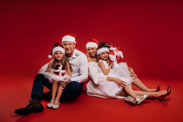 Porträt einer glücklichen Familie in einem Weihnachtshut auf rotem Grund.