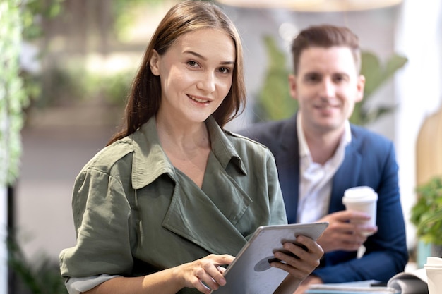 Porträt einer glücklichen Frau, die ein Tablet-Gerät hält und mit Kollegen im Hintergrund an der Theke des Café-Cafés sitzt Concept Business Coffee Time mit intelligenter Technologie funktioniert