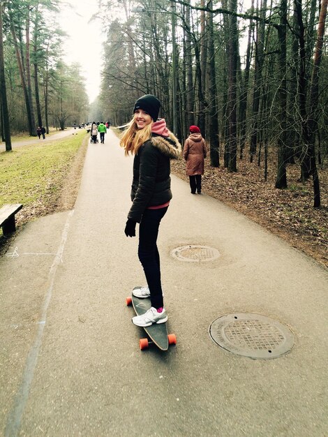 Foto porträt einer glücklichen frau, die inmitten von bäumen auf einem skateboard steht