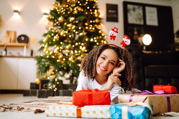 Porträt einer glücklichen Frau, die Winterferien mit großen Geschenkboxen in der Nähe des Weihnachtsbaums feiert.