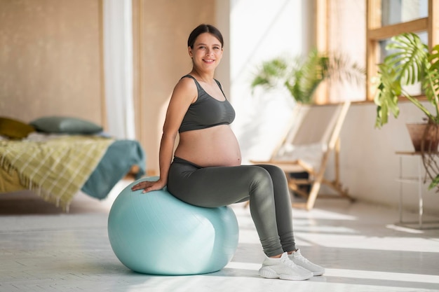 Porträt einer glücklichen Frau, die zu Hause ein Baby erwartet, das auf einem großen Fitball sitzt