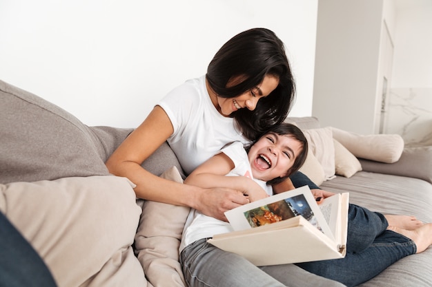 Porträt einer glücklichen Frau mit ihrer kleinen Tochter, die herum spielt und Spaß hat, während sie zu Hause ruht