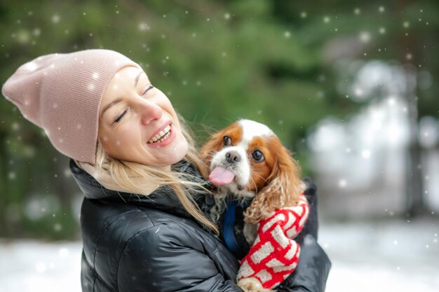 Foto porträt einer glücklichen frau und eines spaniel-hundes im winterwald. frau hält den niedlichen kleinen spaniel-wal in den händen