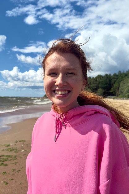 Porträt einer glücklichen, fröhlichen jungen Frau, die an Sommer- oder Herbsttagen draußen am Strand spaziert und sich entspannt
