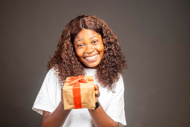 Porträt einer glücklichen hübschen Afrikanerin, die eine Geschenkbox hält, während sie steht und in die Kamera schaut