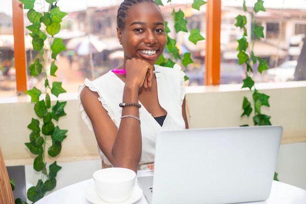 Porträt einer glücklichen jungen afrikanischen Frau, die sich im Café im Freien entspannt und einen Laptop benutzt