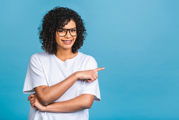 Porträt einer glücklichen jungen Afroamerikanerfrau, die Finger weg auf Kopienraum lokalisiert über blauem Hintergrund zeigt.