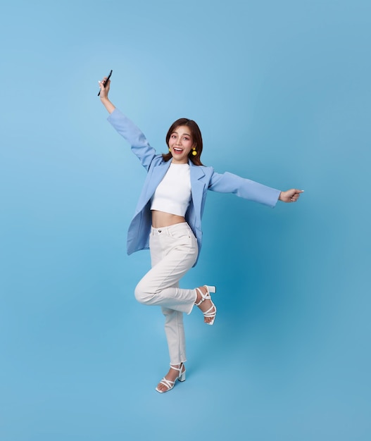 Porträt einer glücklichen jungen asiatischen Frau, die mit einem Mobiltelefon über blauem Hintergrund feiert