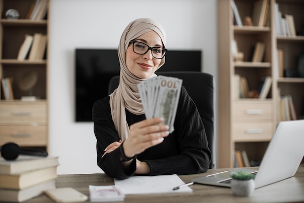 Porträt einer glücklichen jungen attraktiven muslimischen Buchhalterin mit Bargeldbanknoten