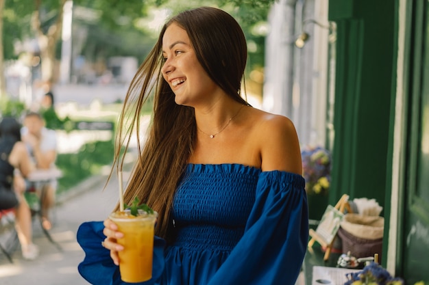 Porträt einer glücklichen jungen Frau, die blaues Kleid trägt und Sommercocktaillimonade trinkt