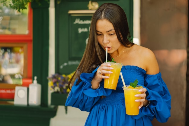 Porträt einer glücklichen jungen Frau, die blaues Kleid trägt und Sommercocktaillimonade trinkt