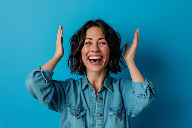 Porträt einer glücklichen jungen Frau mit erhobenen Händen vor blauem Hintergrund stockfoto
