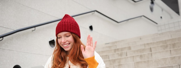 Foto porträt einer glücklichen jungen rothaarigen frau mit laptop, die mit der hand winkt und im video-chat „hallo“ sagt