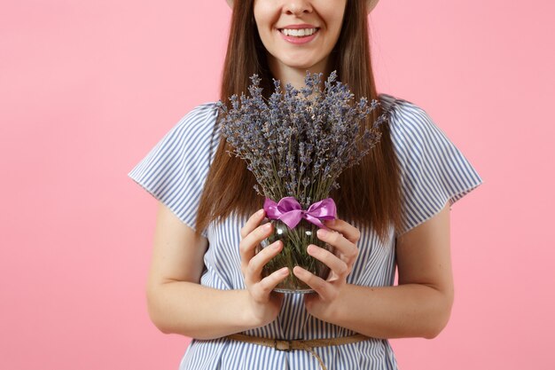 Porträt einer glücklichen jungen zarten Frau in blauem Kleid, Hut, der einen Strauß schöner lila Lavendelblüten hält, einzeln auf hellem rosafarbenem Hintergrund. Feiertagskonzept zum Internationalen Frauentag.