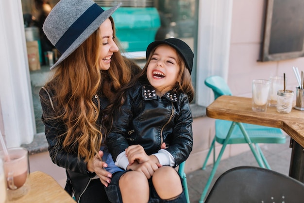 Porträt einer glücklichen liebevollen Familie, Mutter und Tochter, die im Stadtcafé spielen und umarmen. Mutter und Tochter lachen aufrichtig. Styling Familie, wahre Emotionen, guten Tag.