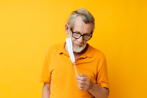 Porträt einer glücklichen medizinischen Maske eines älteren Mannes in einem gelben Hemd, isolierter Hintergrund