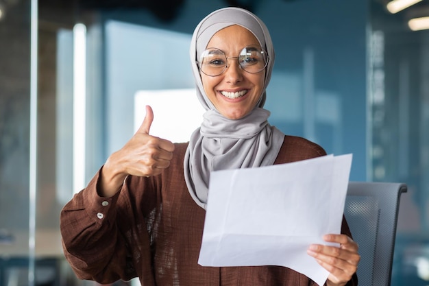 Porträt einer glücklichen muslimischen Frau in einem Hijab, einer Studentin, die ein Dokument hält, einen Brief, ein Blatt Papier