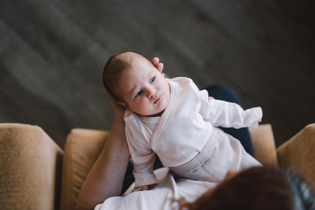 Porträt einer glücklichen Mutter, die ein Kleinkind an den Händen hält Liebevolle Mutter, die zu Hause ihr neugeborenes Baby trägt Mutter umarmt ihr kleines 1 Monate altes Mädchen