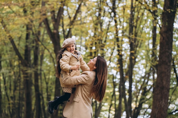 Porträt einer glücklichen Mutter und Tochter, die gemeinsam Zeit im Herbstpark mit fallenden gelben Blättern verbringen