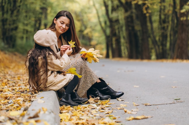 Porträt einer glücklichen Mutter und Tochter, die gemeinsam Zeit im Herbstpark mit fallenden gelben Blättern verbringen