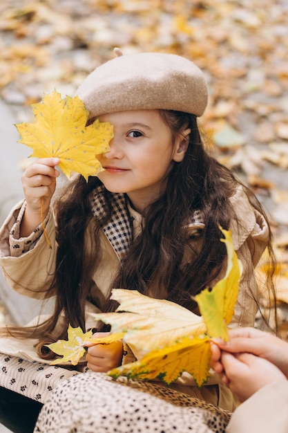 Porträt einer glücklichen Mutter und Tochter, die gemeinsam Zeit im Herbstpark mit fallenden gelben Blättern verbringen