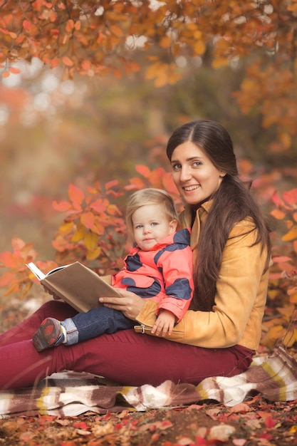 Porträt einer glücklichen Mutter und Tochter, die im Herbstpark ein Buch lesen