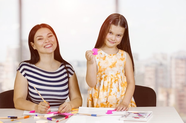 Porträt einer glücklichen Mutter und Tochter mit Bleistiften und Papierbögen zum Zeichnen von verschwommenem Innenhintergrund