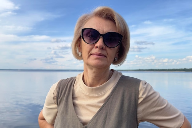 Porträt einer glücklichen schönen älteren älteren Frau in Sonnenbrille, die einen sonnigen Sommertag am Strand genießt