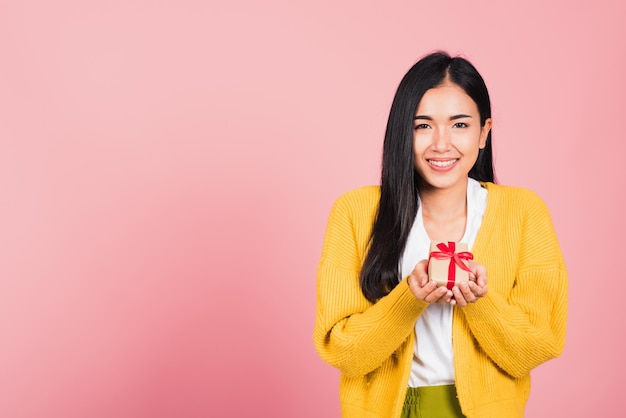 Porträt einer glücklichen, schönen asiatischen jungen Frau, die lächelt und eine kleine Geschenkbox an den Händen hält, Studioaufnahme isoliert auf rosa Hintergrund, Geburtstag, Neujahr, Weihnachten, Valentinstag, Feiertagskonzept