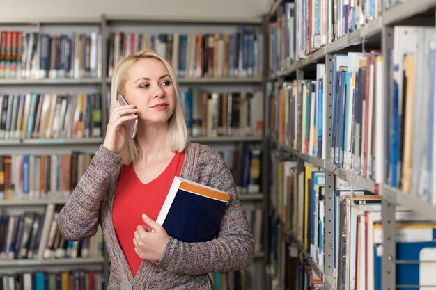 Porträt einer glücklichen schönen Frau, die mit dem Handy in der Bibliothek der Universität spricht