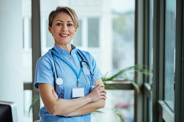 Porträt einer glücklichen, selbstbewussten Krankenschwester, die mit verschränkten Armen im Krankenhaus steht