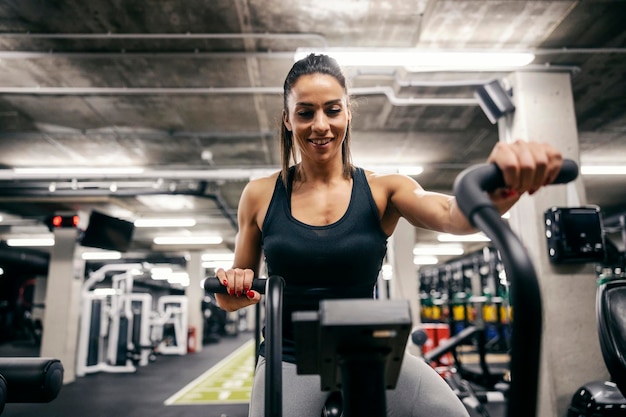 Porträt einer glücklichen Sportlerin, die in einem Fitnessstudio auf einem Ellipsentrainer trainiert