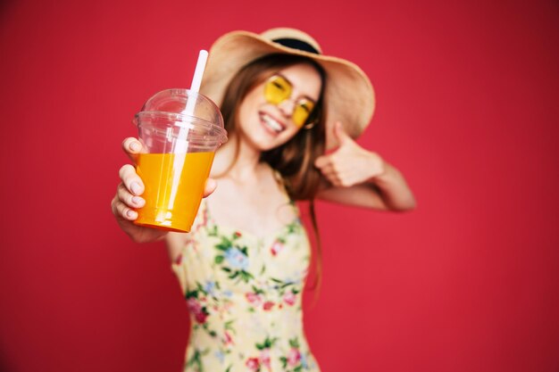 Porträt einer glücklichen und aufgeregten blonden trendigen Frau mit Hut mit frischem Getränk in den Händen isoliert auf rosa Hintergrund. Sommerstimmung