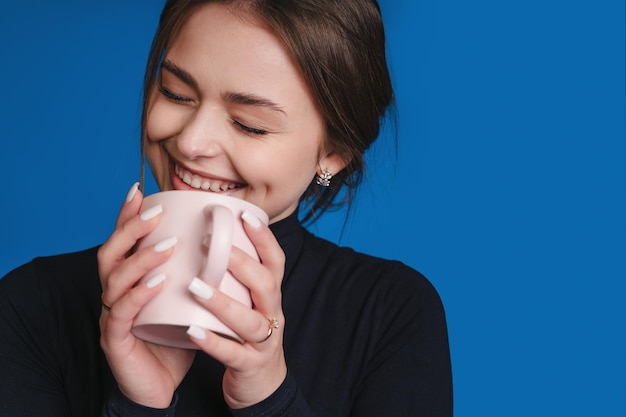 Porträt einer hübschen Frau, die Freizeit hat und eine Tasse Kaffee isoliert auf blauem Hintergrund hält