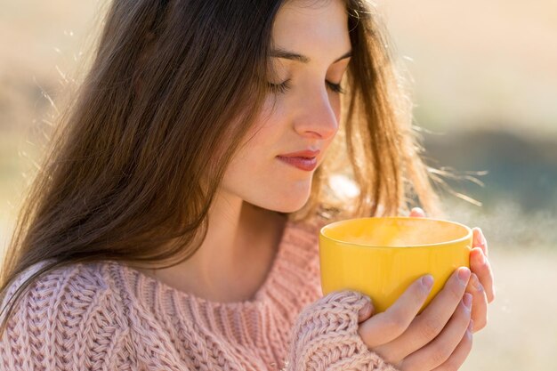 Porträt einer hübschen jungen Frau im stilvollen Strickpullover, die an einem sonnigen Tag auf dem goldenen Herbstwald steht