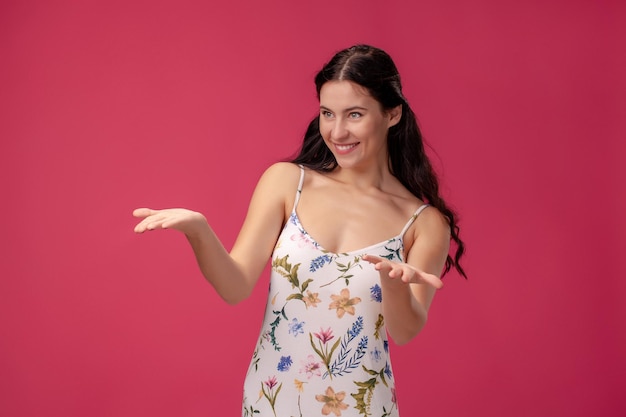 Porträt einer hübschen jungen Frau in einem hellen Kleid, das auf rosafarbenem Hintergrund im Studio steht. Menschen aufrichtige Emotionen.