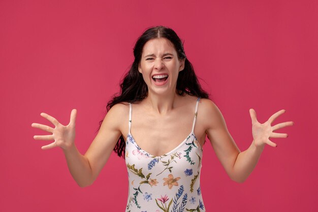 Porträt einer hübschen jungen Frau in einem hellen Kleid, die auf rosa Hintergrund in Studioleuten steht, seit...