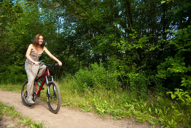 Foto porträt einer hübschen jungen frau mit fahrrad in einem park lächelnd - outdoor