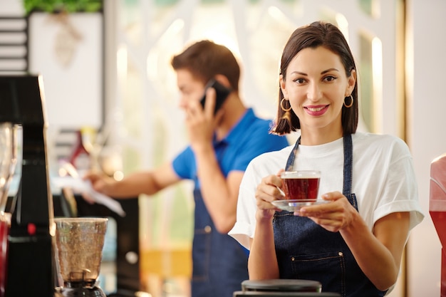 Porträt einer hübschen lächelnden Barista, die eine Tasse köstlichen frischen Kaffee hält