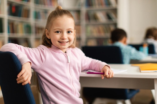 Porträt einer hübschen Schülerin, die am Schreibtisch im Klassenzimmer sitzt, sich umdreht und lächelt