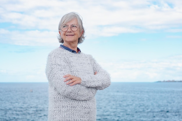 Porträt einer hübschen Seniorin, die mit verschränkten Armen am Meer steht Lächelnde ältere Dame