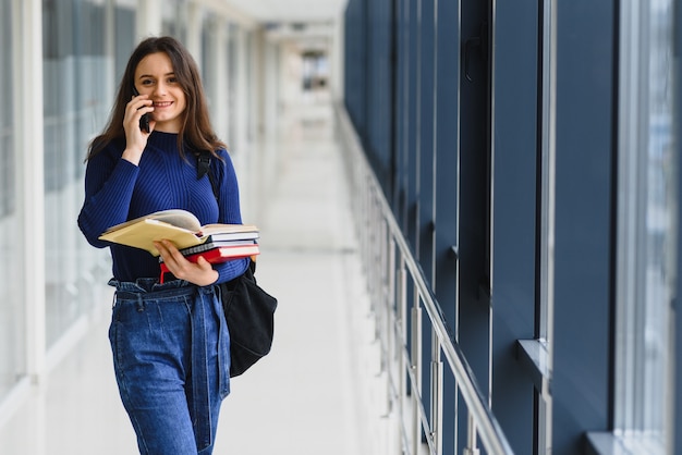 Porträt einer hübschen Studentin mit Büchern und einem Rucksack im Flur der Universität