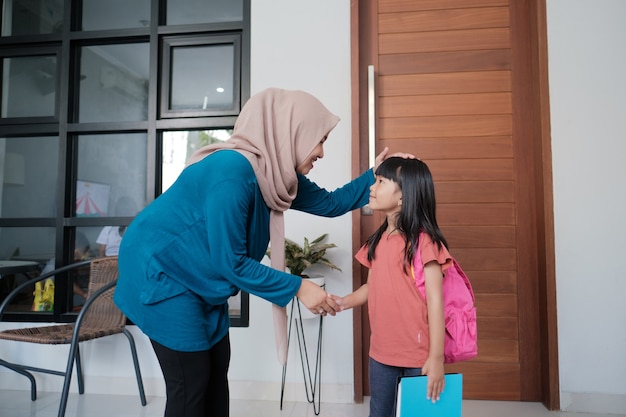 Porträt einer indonesischen Grundschulstudentin schütteln und küssen die Hand ihrer muslimischen Mutter, bevor sie zur Schule geht