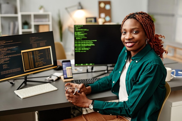 Porträt einer it-entwicklerin, die in die kamera schaut und gegen den programmcode auf computern lächelt